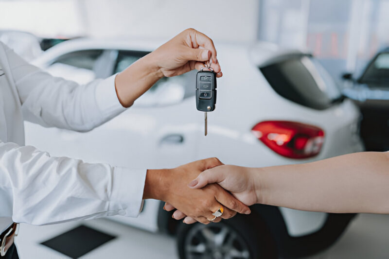 Customer receiving car keys from dealership after buying a new vehicle – handshake and car handover concept.