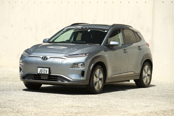 A silver Hyundai Kona Electric SUV parked outdoors on a sunny day, showcasing its sleek front design and aerodynamic body.