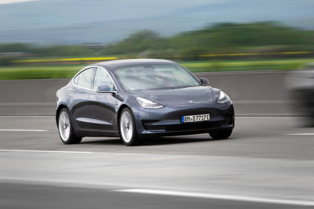 A dark gray Tesla Model 3 electric car driving at high speed on a highway