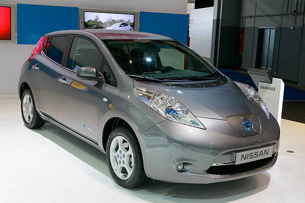 "A silver Nissan Leaf electric car on display at an auto show, highlighting its compact hatchback design